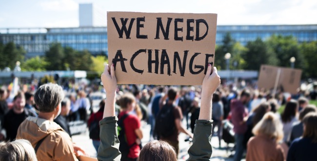 A rear view of people with placards and posters that say we need a change.