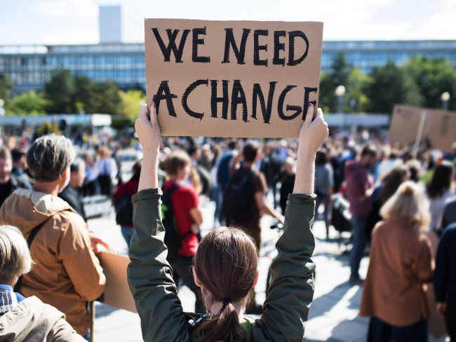 A rear view of people with placards and posters that say we need a change.